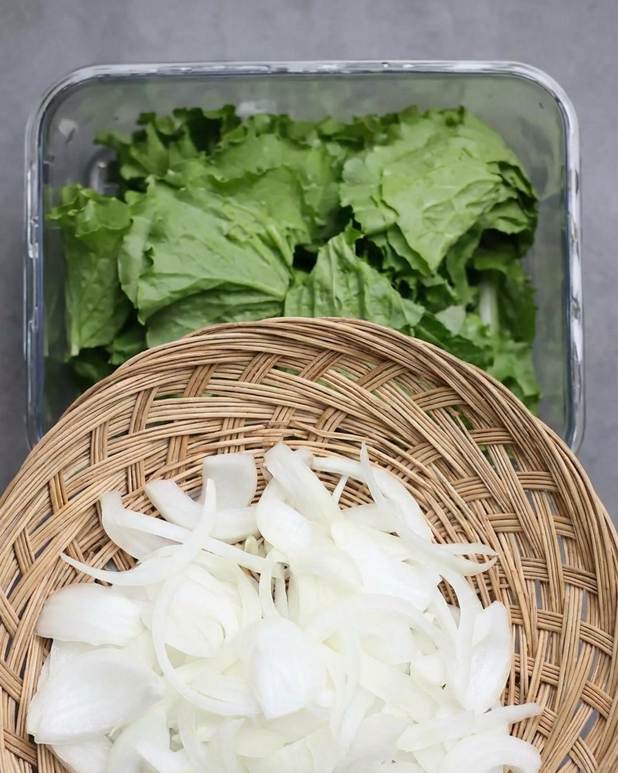 Oignons émincés parsemés sur les feuilles de laitue dans un bac de conservation en verre.