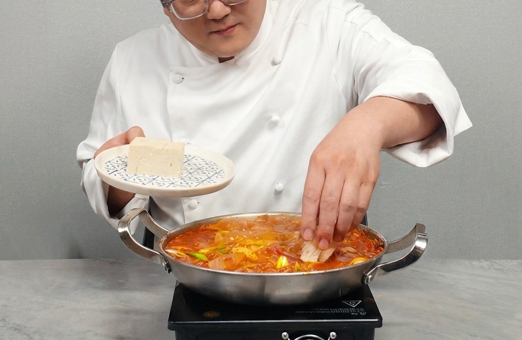Une personne disposant des tranches de tofu blanc ferme dans le bouillon rouge piquant.
