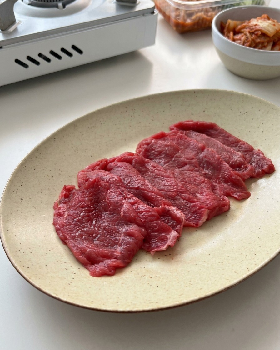 Tranches de bœuf cru émincées disposées sur une assiette en céramique mouchetée.