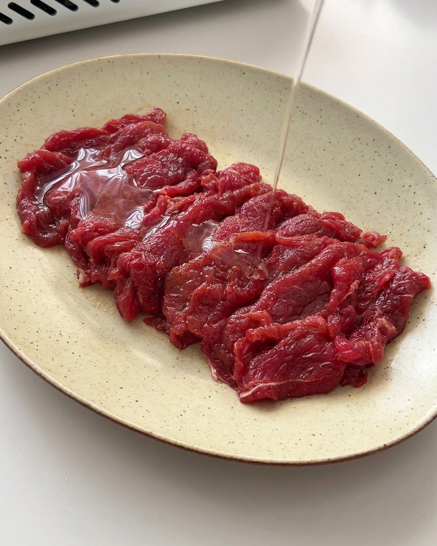Un filet dhuile de cuisson versé sur les tranches de bœuf marinées.