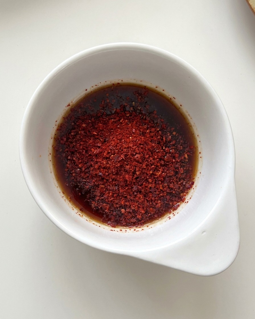 Petit bol blanc contenant un mélange de sauce soja et de poudre de piment rouge vif.