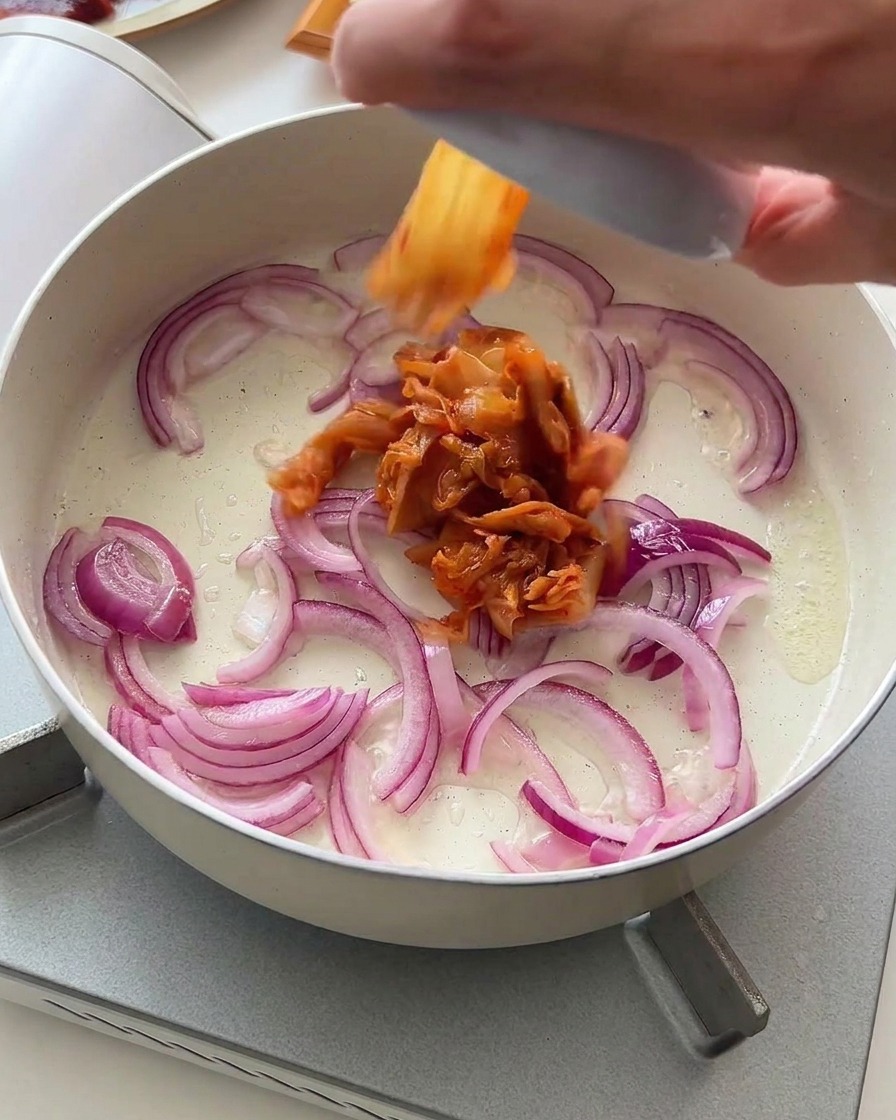 Morceaux de kimchi ajoutés dans la poêle avec les oignons rouges en train de dorer.