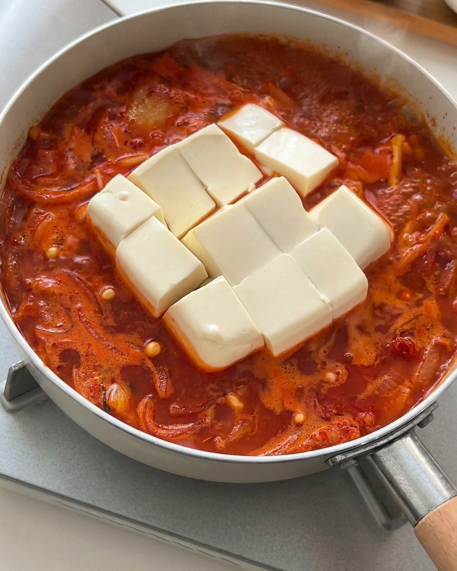Bloc de tofu soyeux blanc coupé en dés placé délicatement dans le ragoût de kimchi bouillonnant.