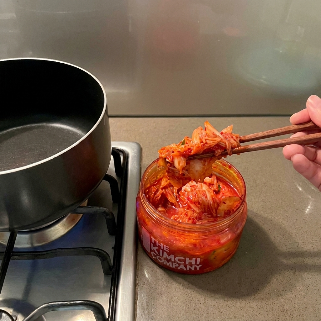 Une main utilisant des baguettes en bois pour sortir du kimchi rouge vif dun bocal au-dessus dune marmite vide.
