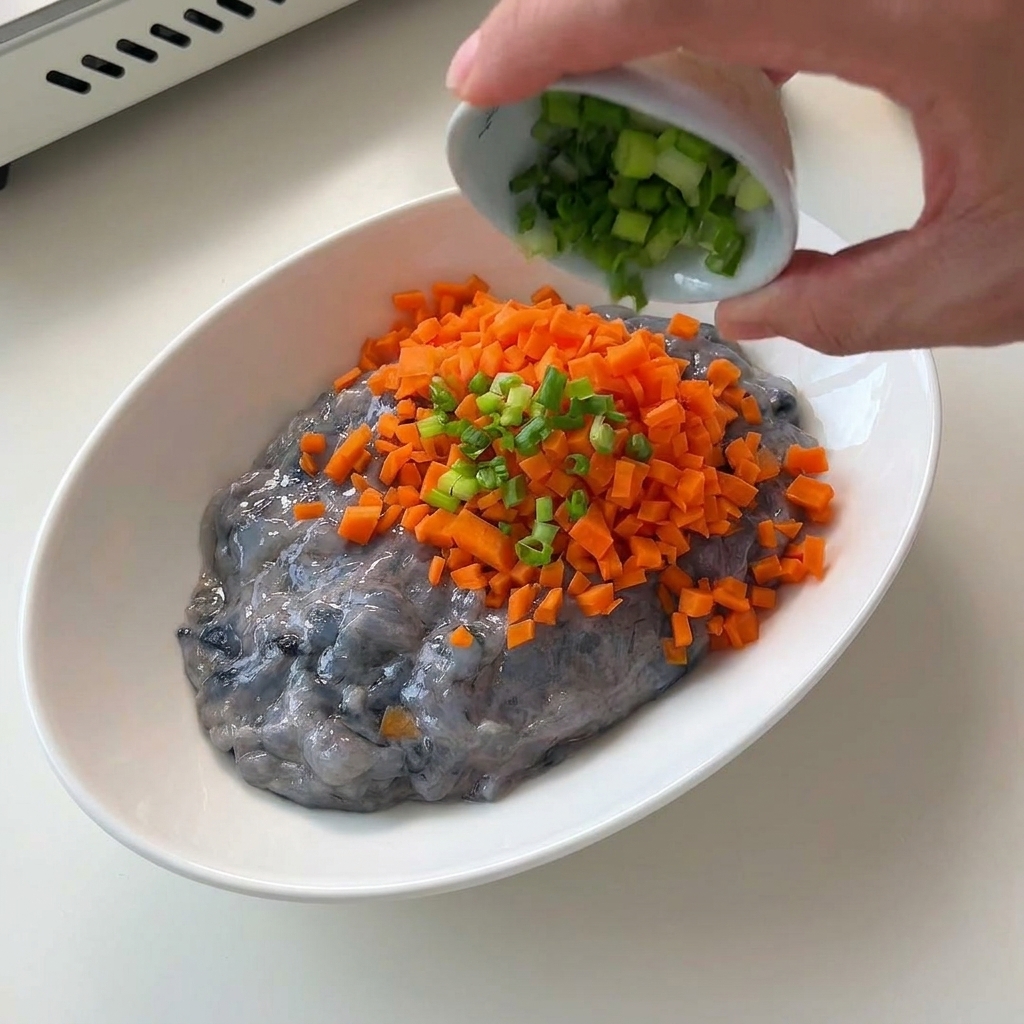 Des dés de carottes orange finement coupés sont versés dans un bol blanc contenant une pâte de crevettes crues et translucide.