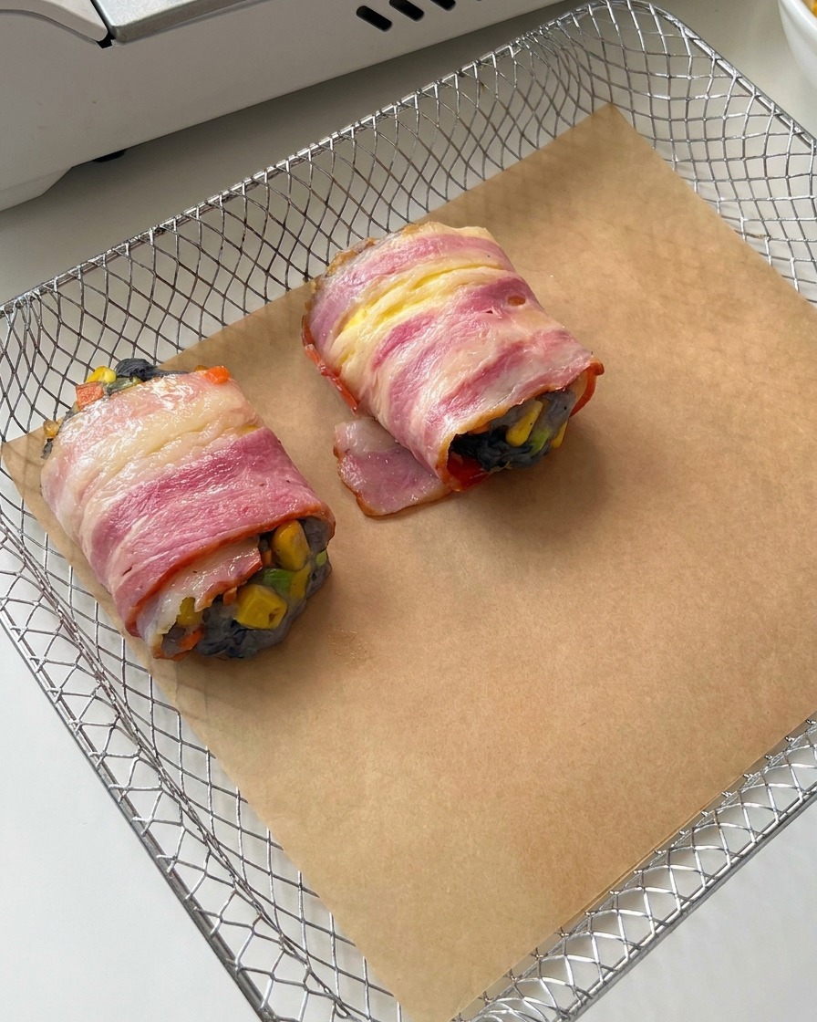 Deux rouleaux crus de crevettes enrobés de lard reposant sur du papier sulfurisé marron dans le panier en métal dune friteuse à air.