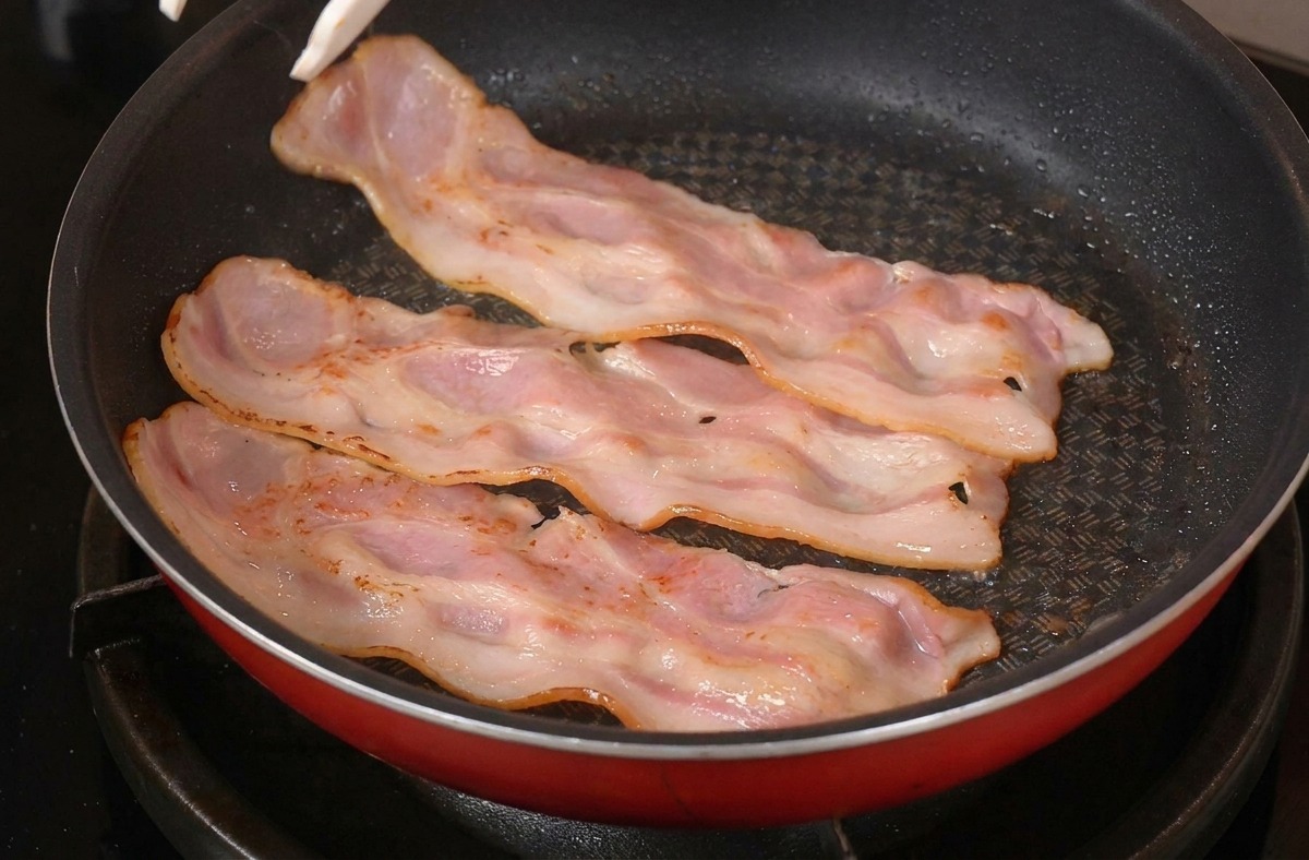 Utilisation dune pince pour retourner les tranches de bacon dorées dans une poêle rouge.