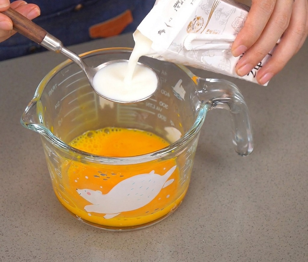 Versement dun peu de lait dans une cuillère au-dessus des œufs battus.