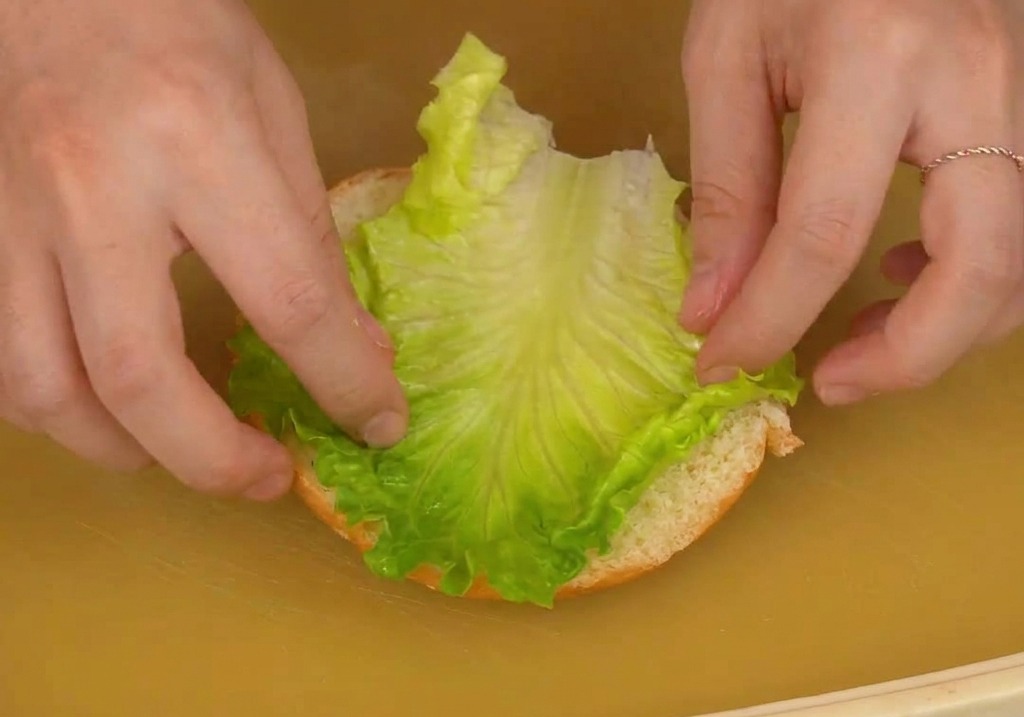 Mains déposant une feuille de laitue croquante sur la base dun pain burger.