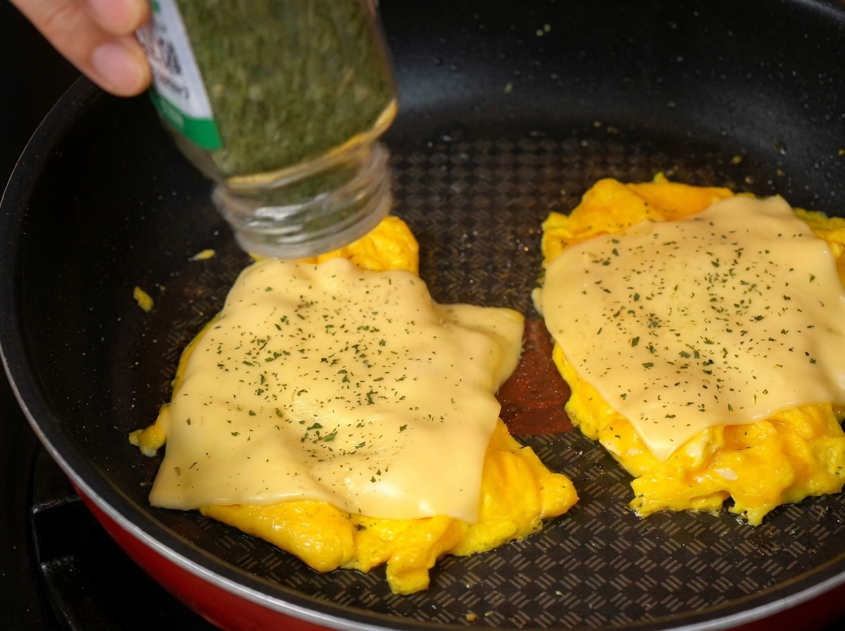 Saupoudrage de persil séché sur les œufs au fromage fondu dans la poêle.