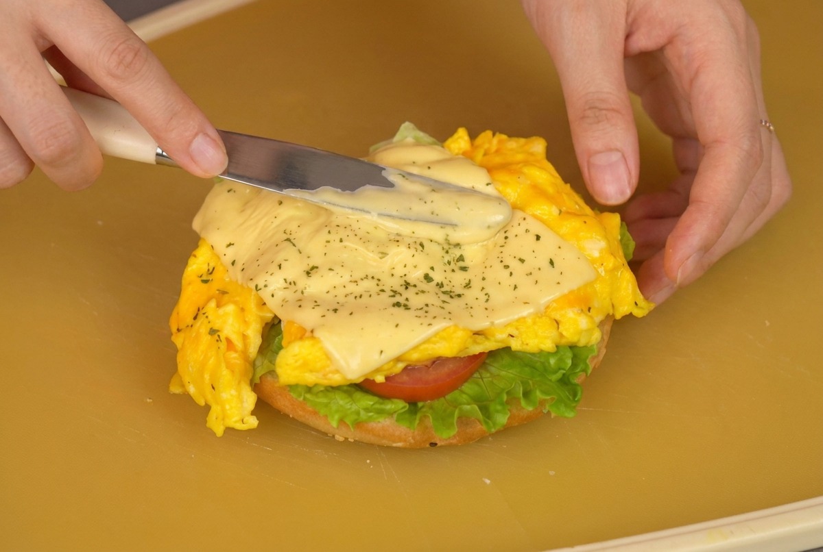 Utilisation dune spatule pour transférer les œufs au fromage sur le pain garni de laitue et tomate.