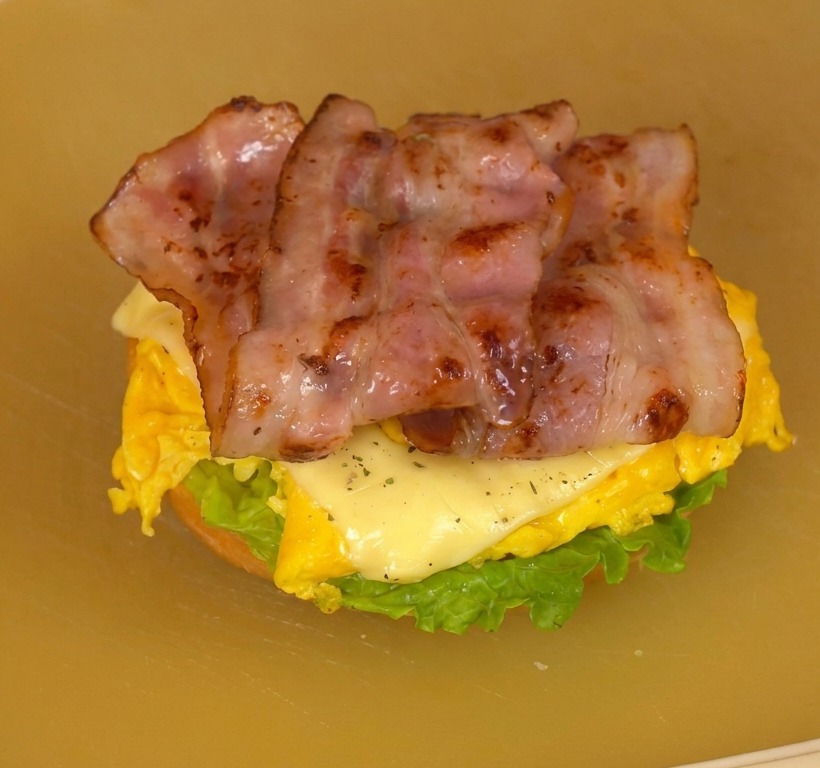 Burger ouvert montrant les couches de laitue, tomate, œufs fondants et bacon croustillant.