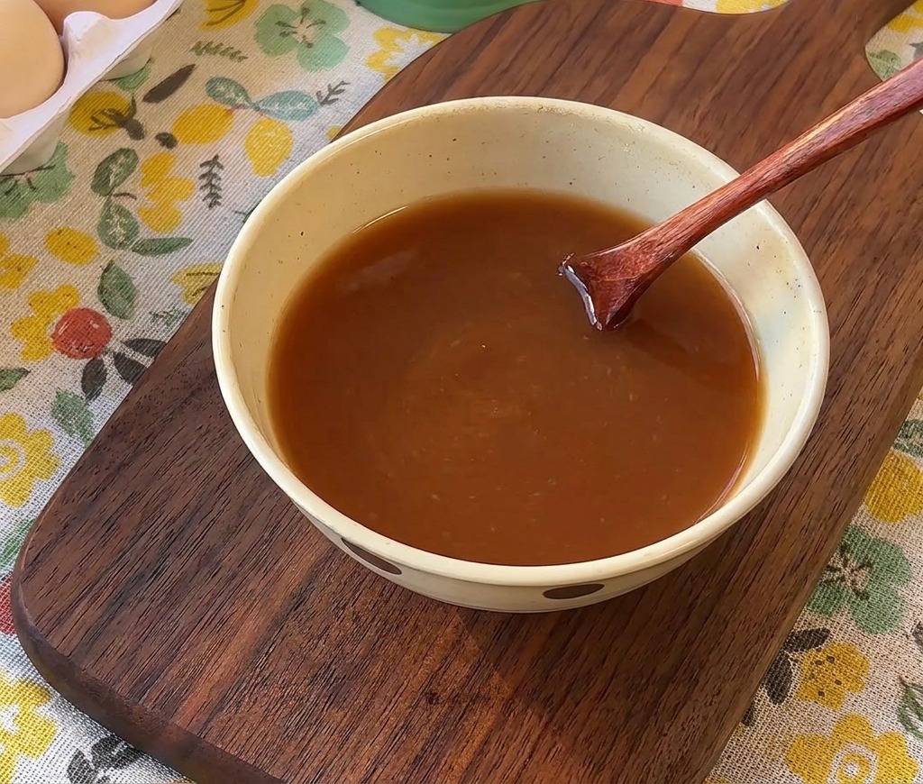 Une cuillère en bois mélangeant une sauce brune liquide dans un bol en céramique.