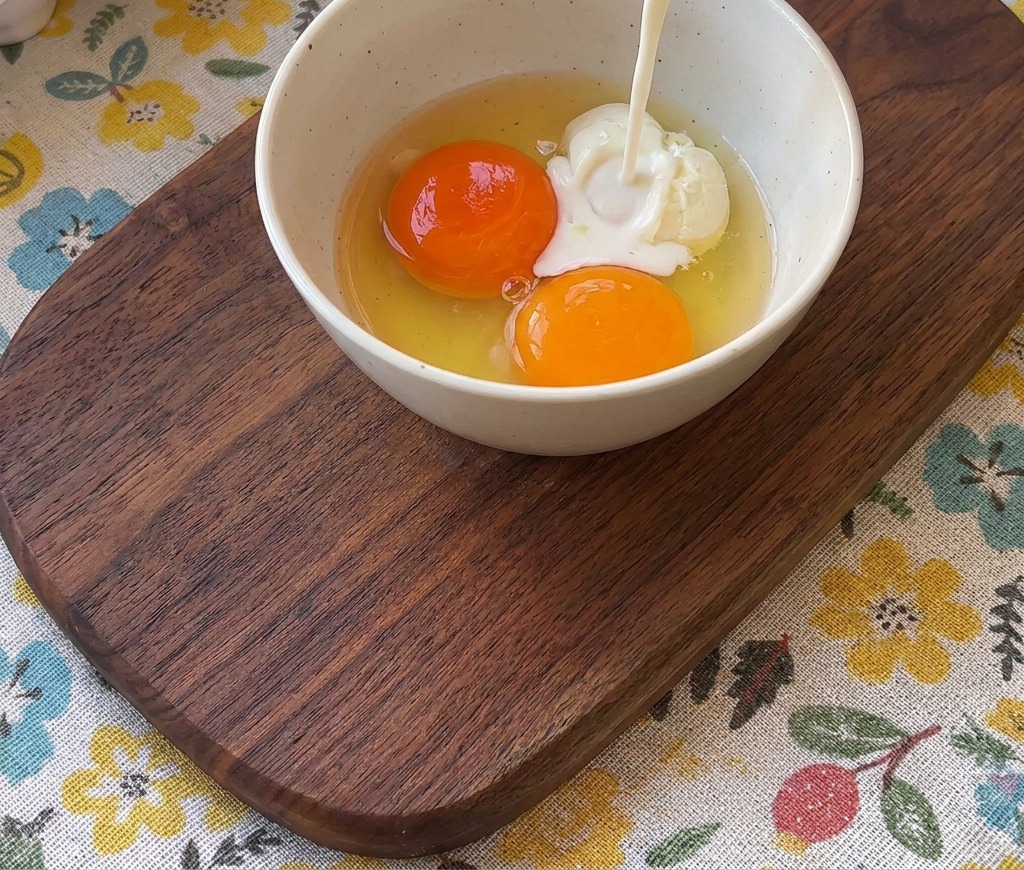 Lait versé dun verre dans un bol contenant deux jaunes dœufs orange vif.