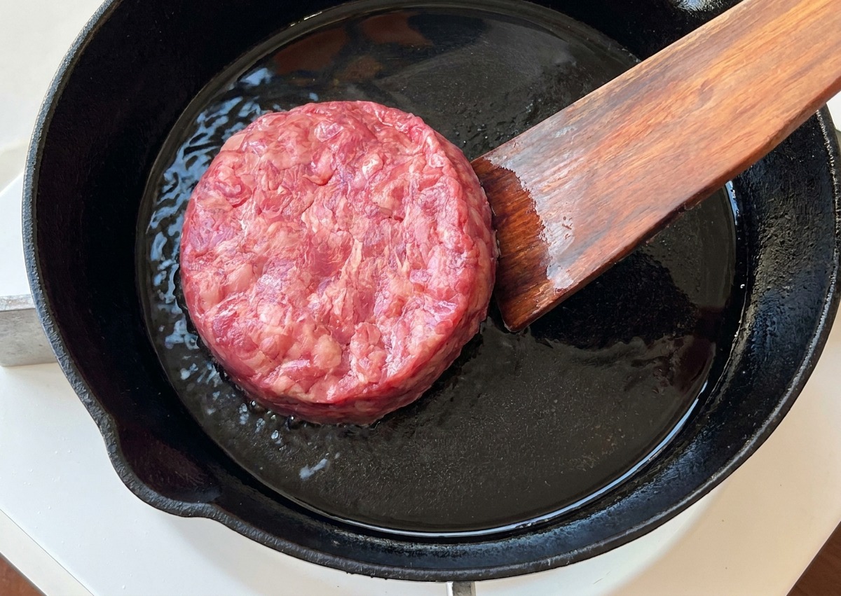 Un steak de bœuf cru déposé dans une poêle en fonte préchauffée avec une spatule en bois.