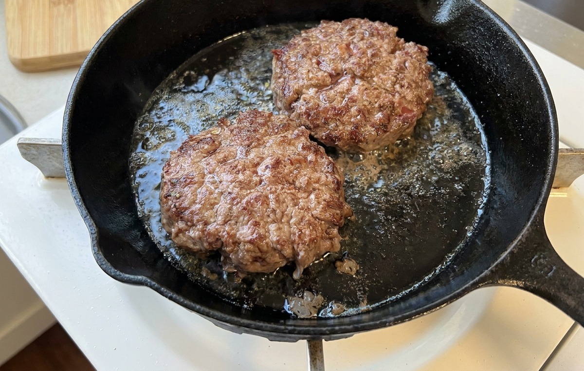 Deux steaks de bœuf grésillant dans une poêle en fonte, montrant une croûte bien brune et caramélisée.