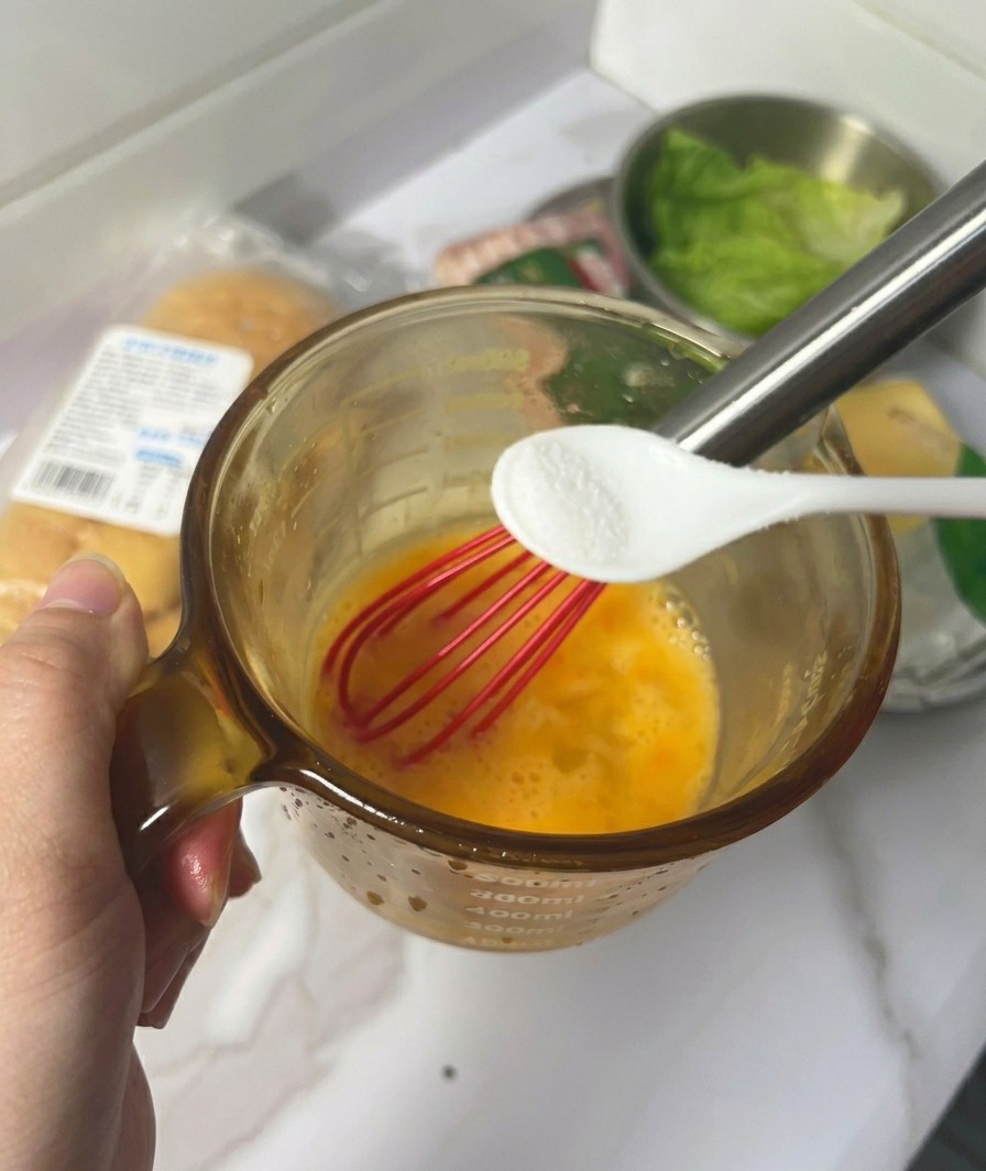 Une main tenant une petite cuillère de sel au-dessus dun verre contenant des œufs battus.