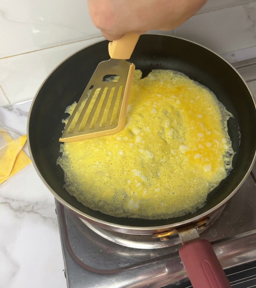Une main utilisant une spatule pour couper une fine omelette en quatre sections dans une poêle.