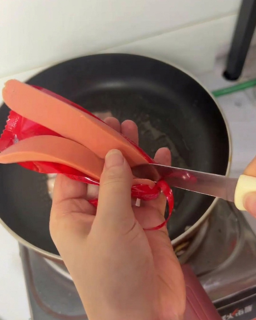 Une personne utilisant un petit couteau pour couper une saucisse hot-dog en deux dans le sens de la longueur.