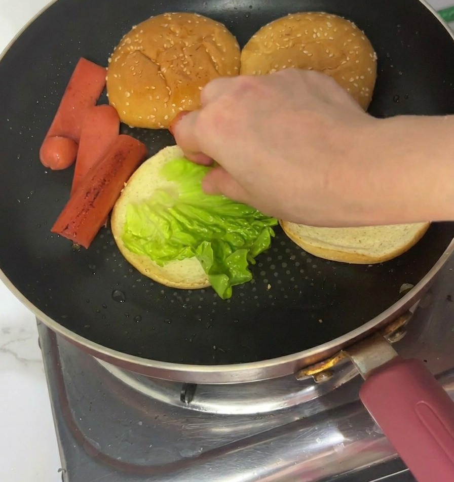 Une main posant une feuille de laitue verte croquante sur la face toastée dun pain à burger.