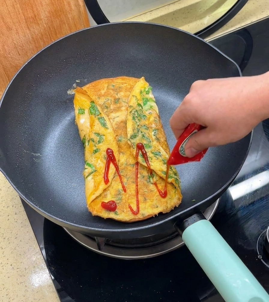 Du ketchup rouge versé dun petit sachet sur une galette dœuf dorée pliée dans une poêle.