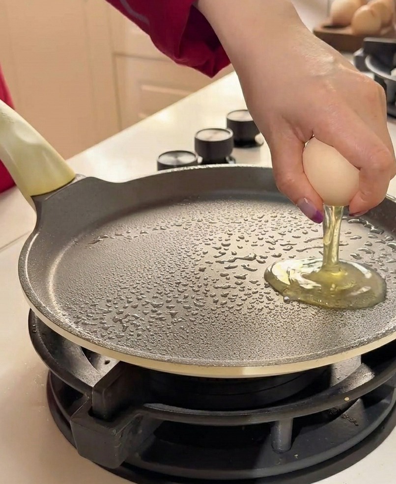 Deux œufs crus cassés sur une poêle plate graissée.
