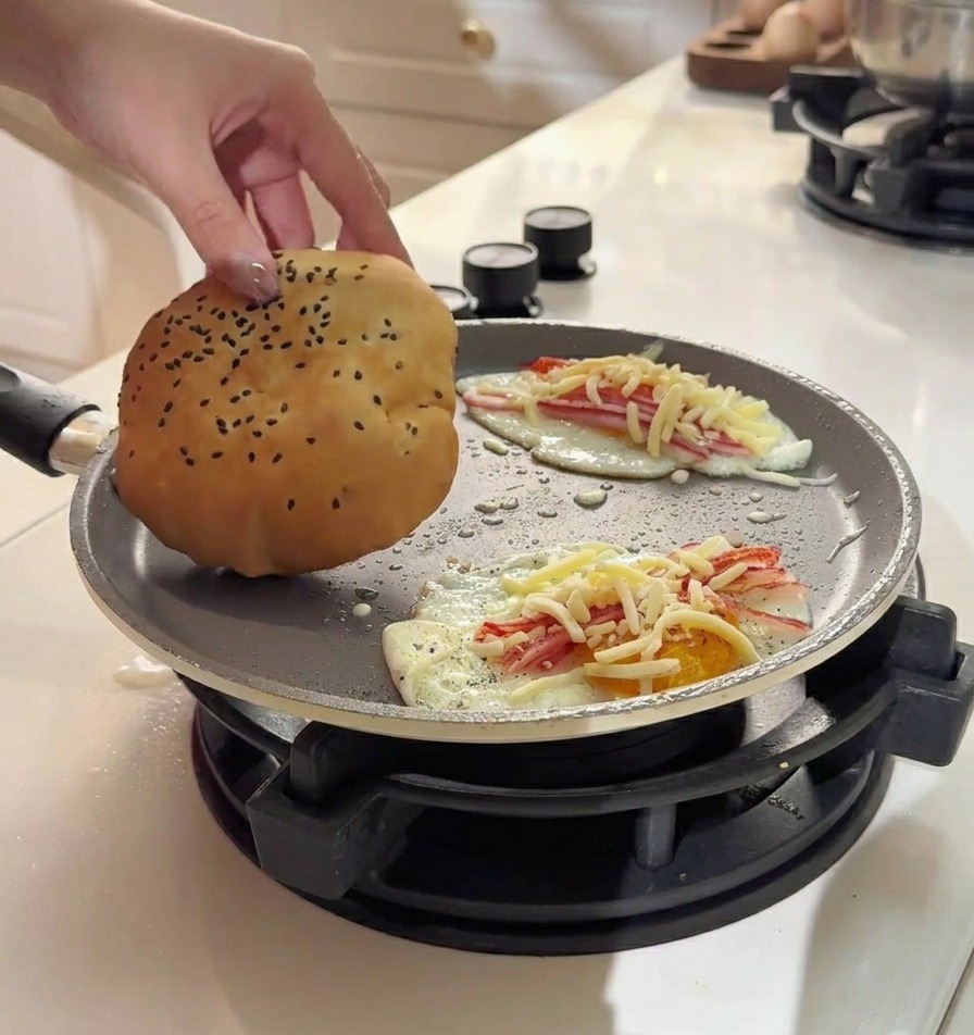 Main plaçant un pain burger doré sur un œuf garni de crabe et de fromage fondu.
