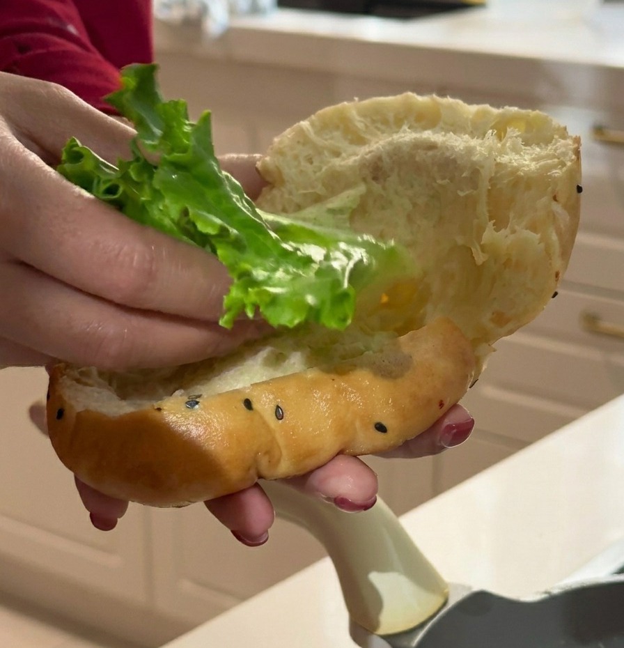 Main insérant une feuille de laitue verte dans le pain burger moelleux.