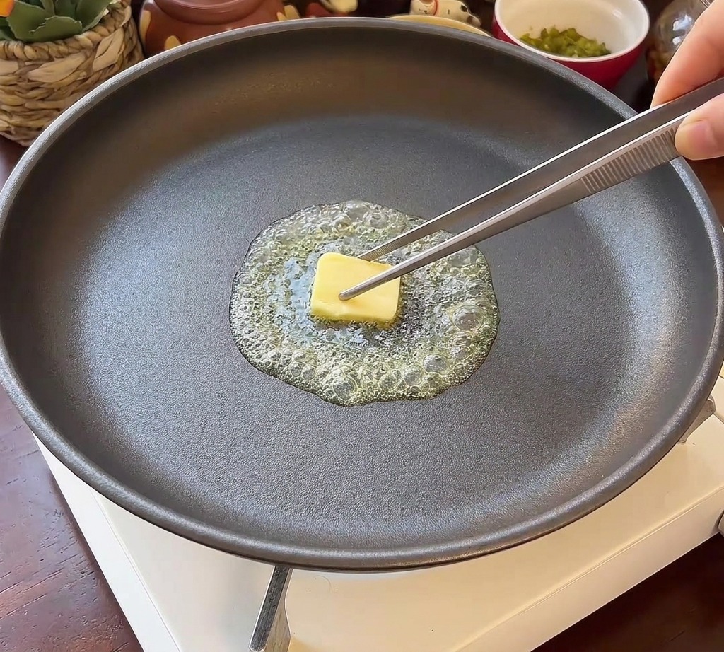Deux moitiés de pain à burger placées face vers le bas dans une poêle sombre avec du beurre fondu frémissant.