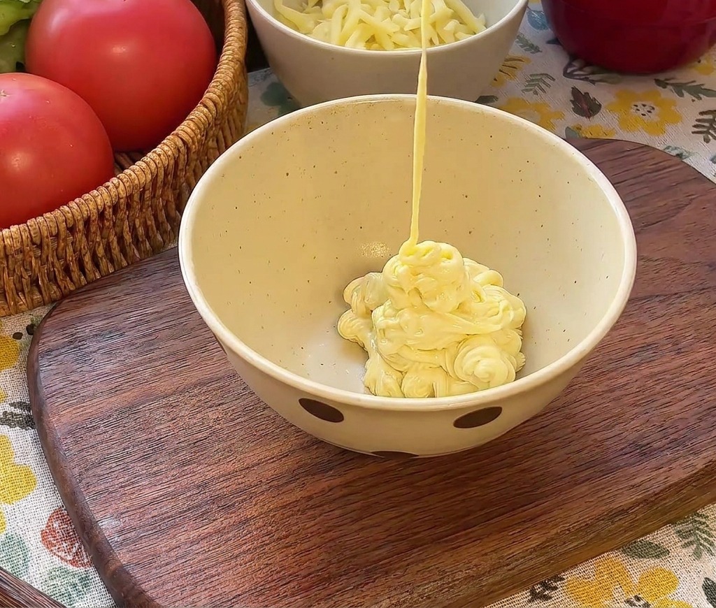 De la mayonnaise crémeuse versée dans un bol sur du ketchup rouge et des cornichons verts hachés.
