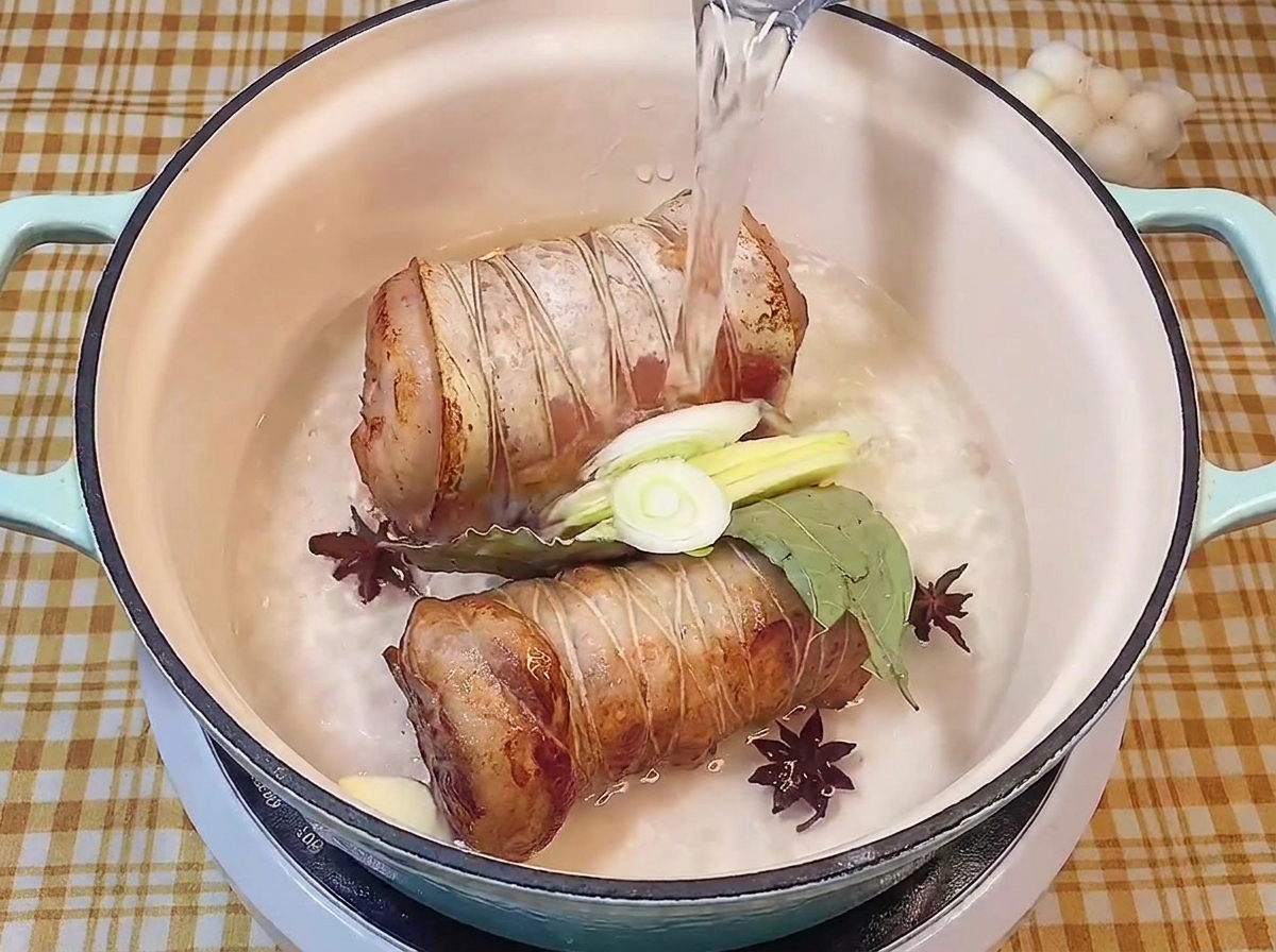 Verser de leau claire dans une marmite contenant les rouleaux de porc, les aromates et les épices.