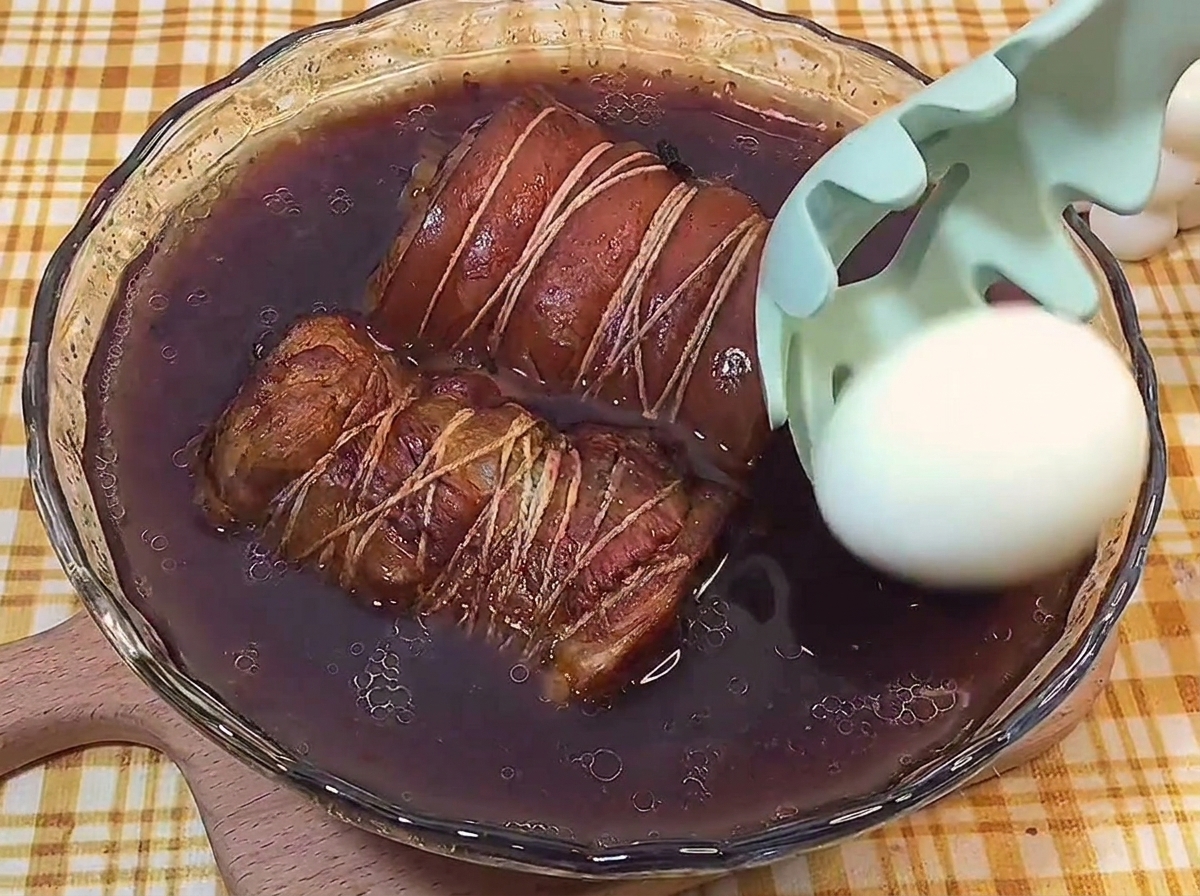 Un œuf dur écalé déposé délicatement dans le jus de braisage sombre avec le porc chashu.