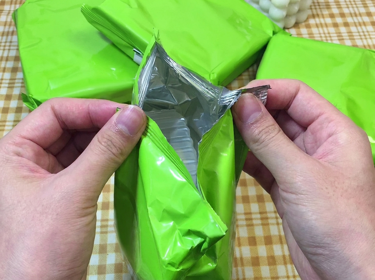 Deux mains déchirant un emballage vert de ramen instantané montrant le bloc de nouilles.