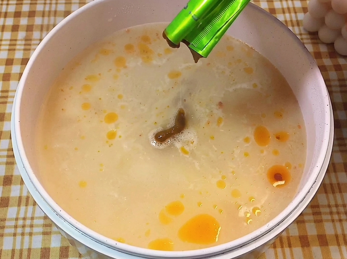 Pâte dassaisonnement brune versée dun sachet vert dans un bouillon frémissant.