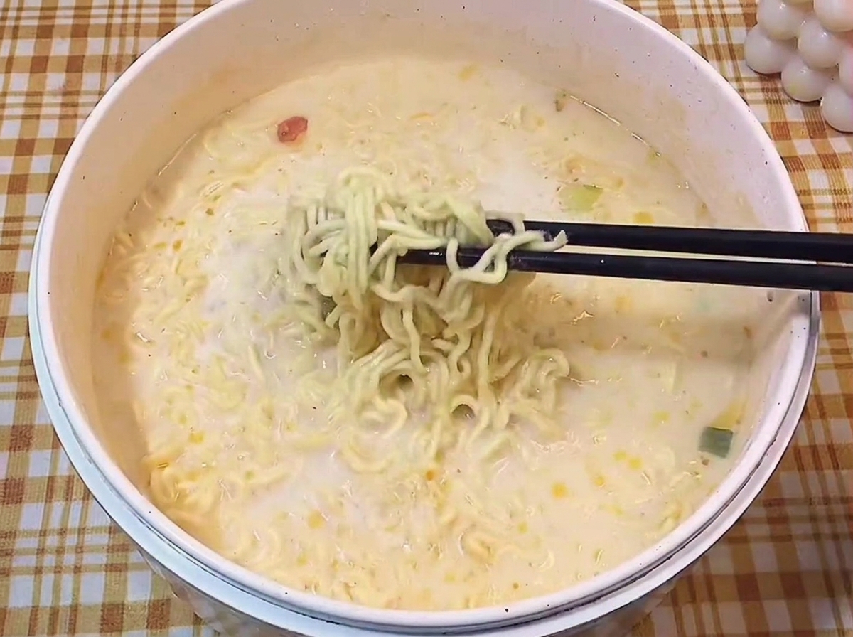 Baguettes noires soulevant des nouilles ramen ondulées hors dun bouillon laiteux.