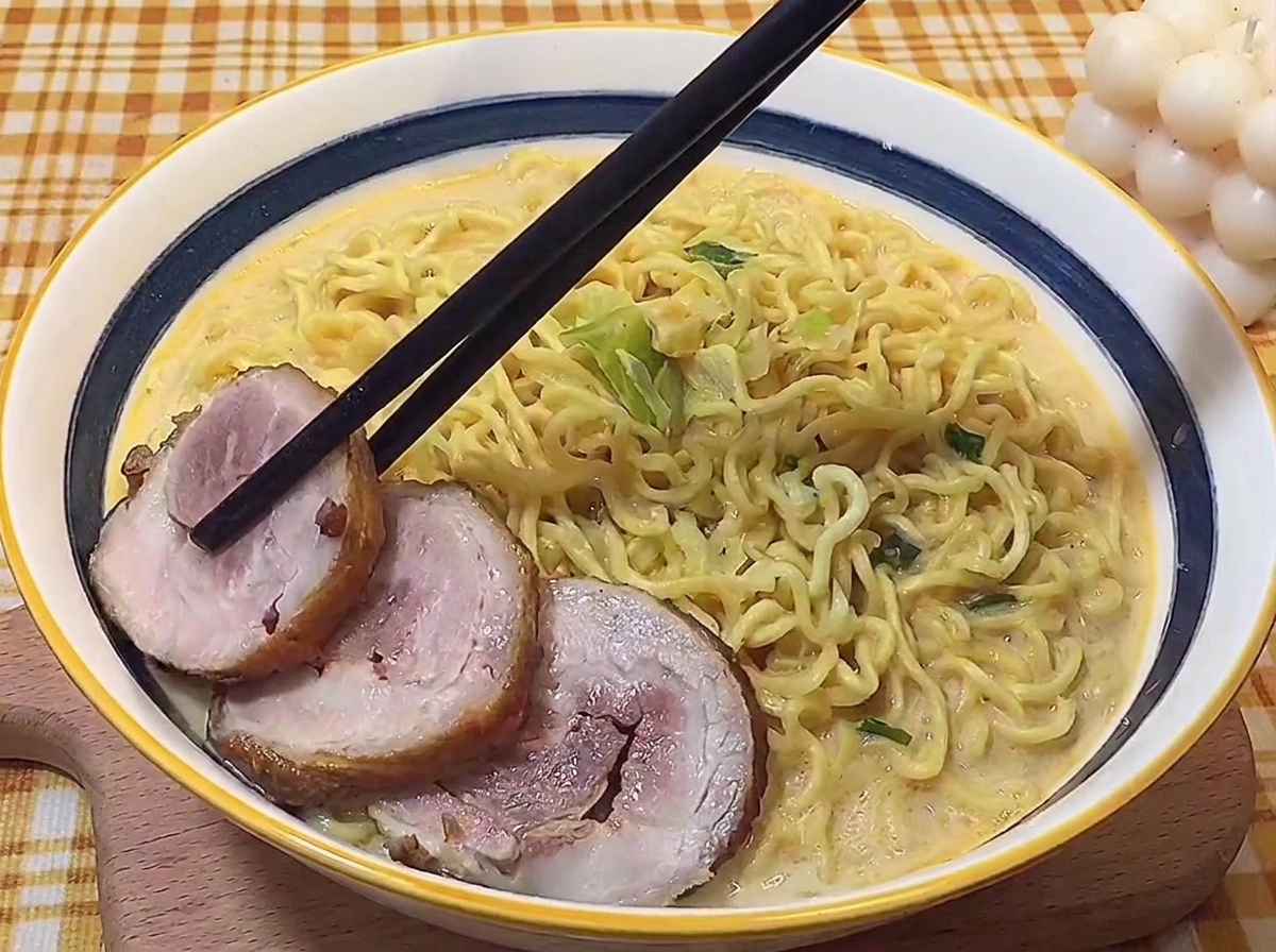 Baguettes déposant soigneusement des tranches de porc braisé dans un bol de ramen tonkotsu.