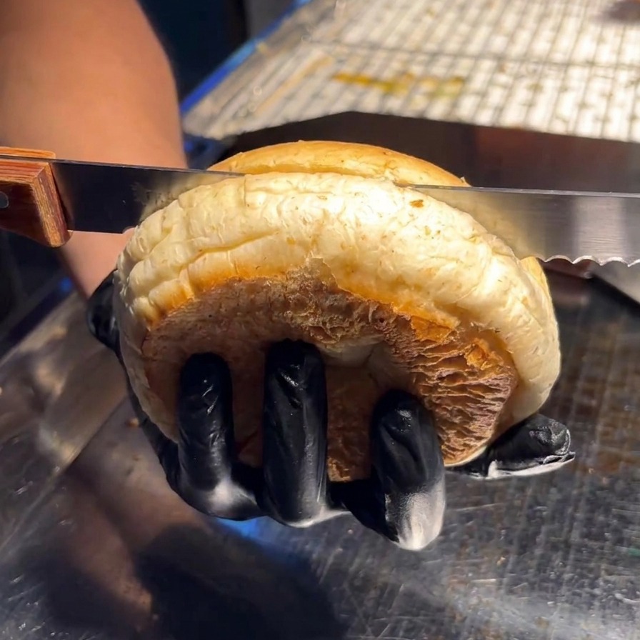 Une personne utilisant un couteau à dents pour couper un grand pain burger moelleux en deux horizontalement.