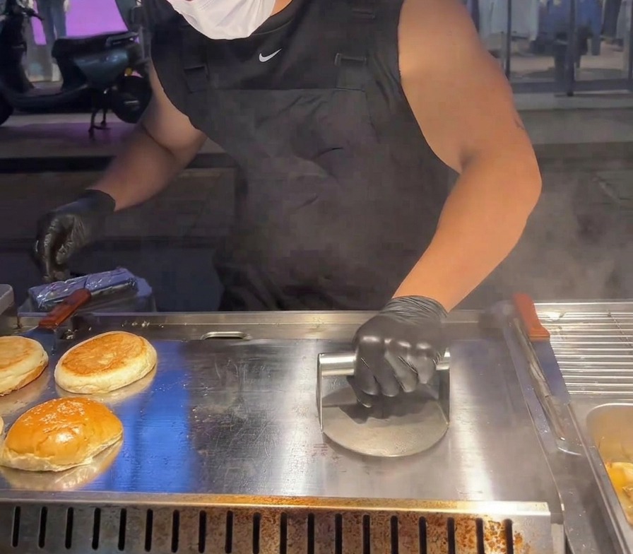 Une presse à burger métallique lourde utilisée pour aplatir un steak de bœuf contre une plaque brûlante.