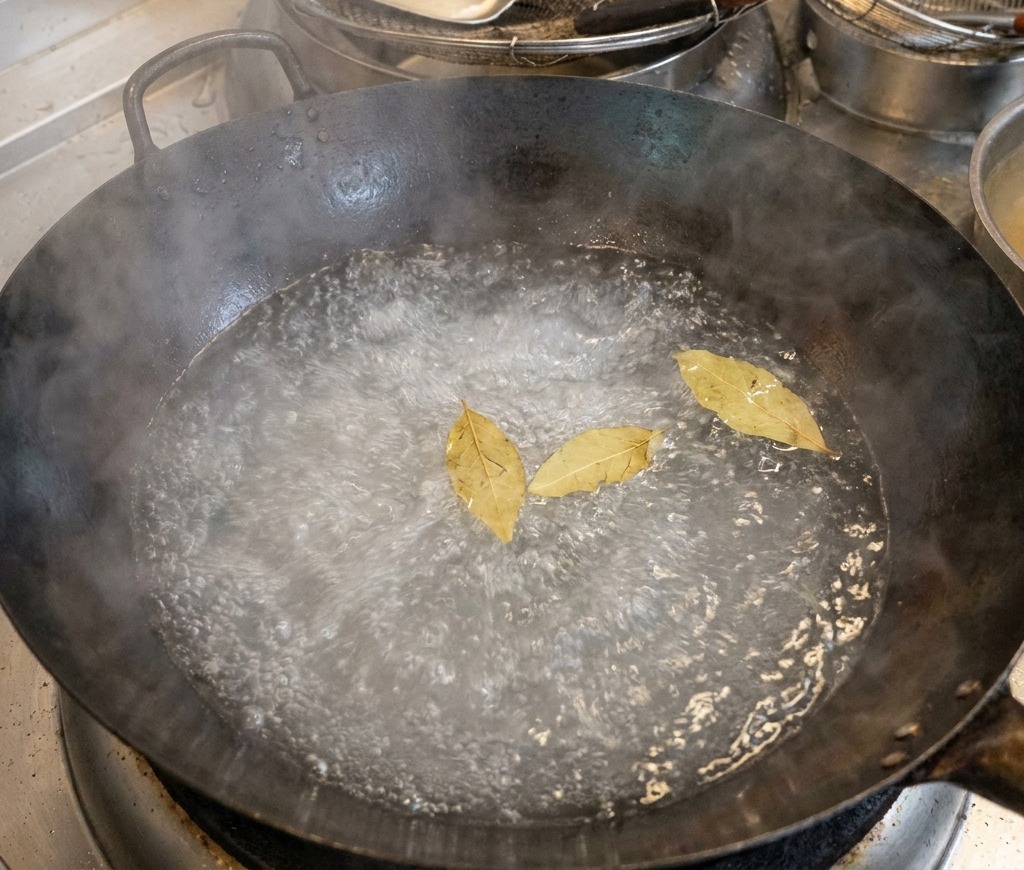 Un grand wok noir rempli deau bouillante avec trois feuilles de laurier flottant à la surface.