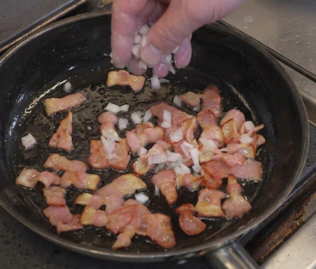 Une main saupoudrant de loignon haché sur des tranches de bacon partiellement cuites.