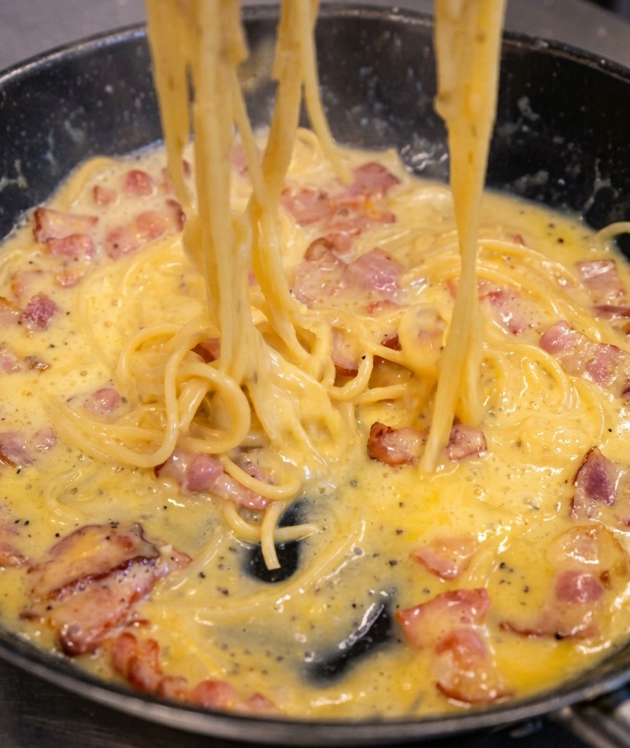 Spaghetti mélangés dans la poêle, montrant la sauce devenant onctueuse et nappant parfaitement les pâtes.