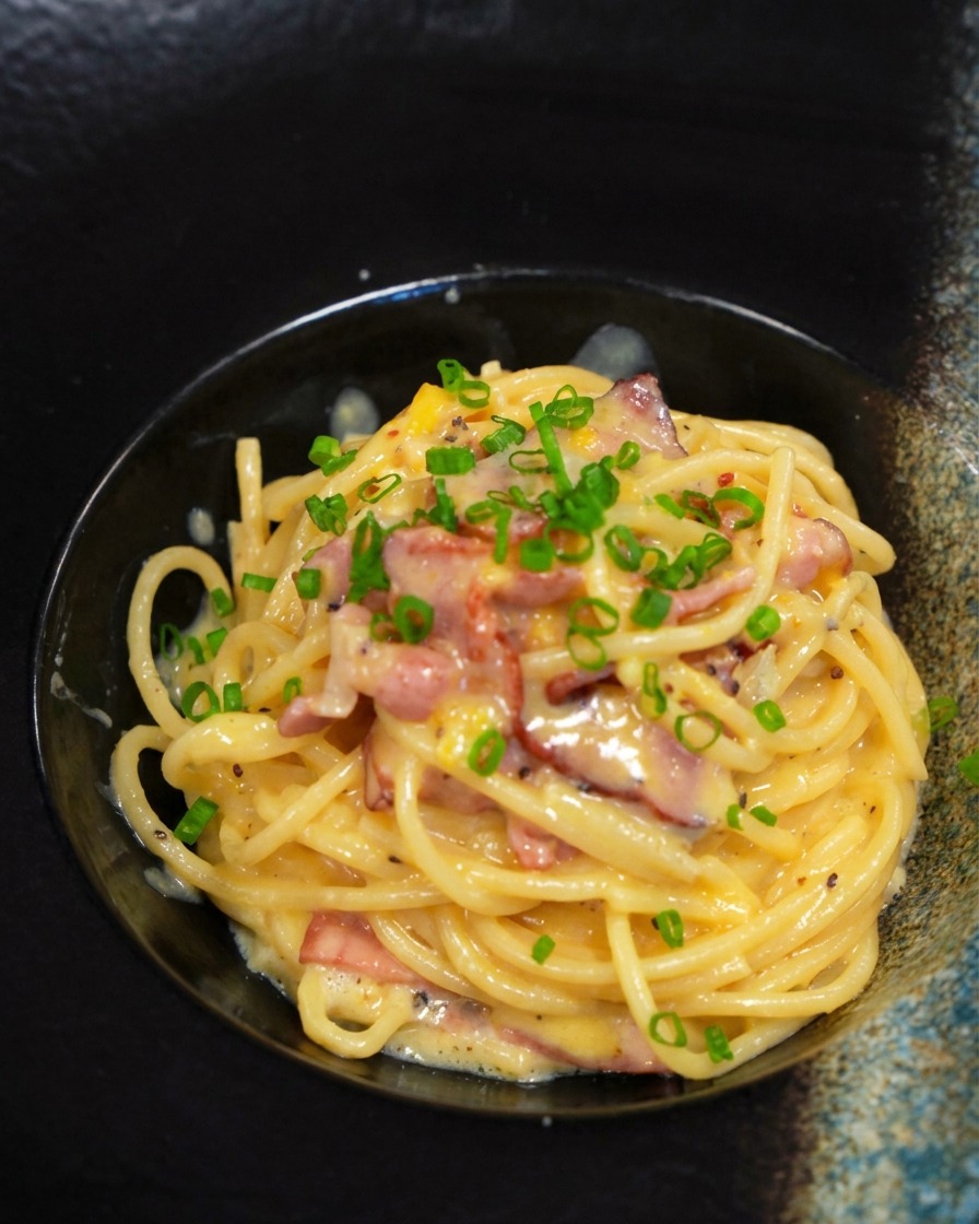 Une portion de carbonara dans un bol noir décorée de ciboulette ciselée vert vif.
