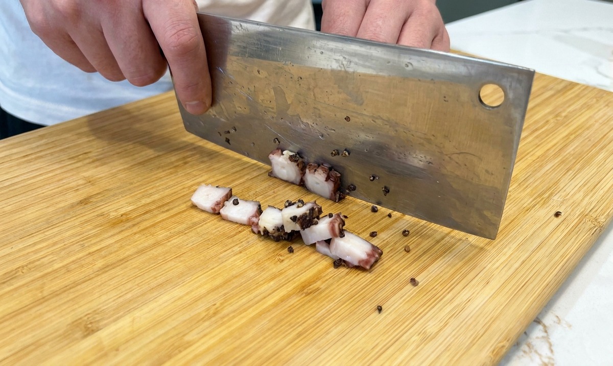 Tranchage du guanciale en petits dés avec un couteau sur une planche en bois.