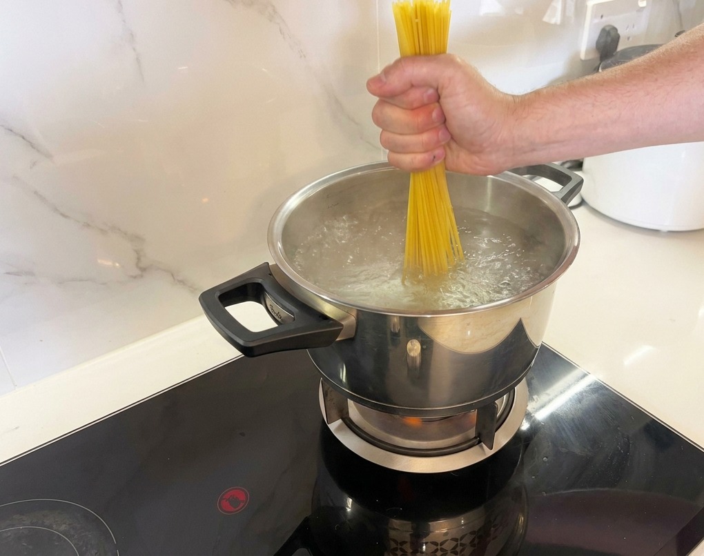 Une main plongeant des spaghetti secs dans leau bouillante.