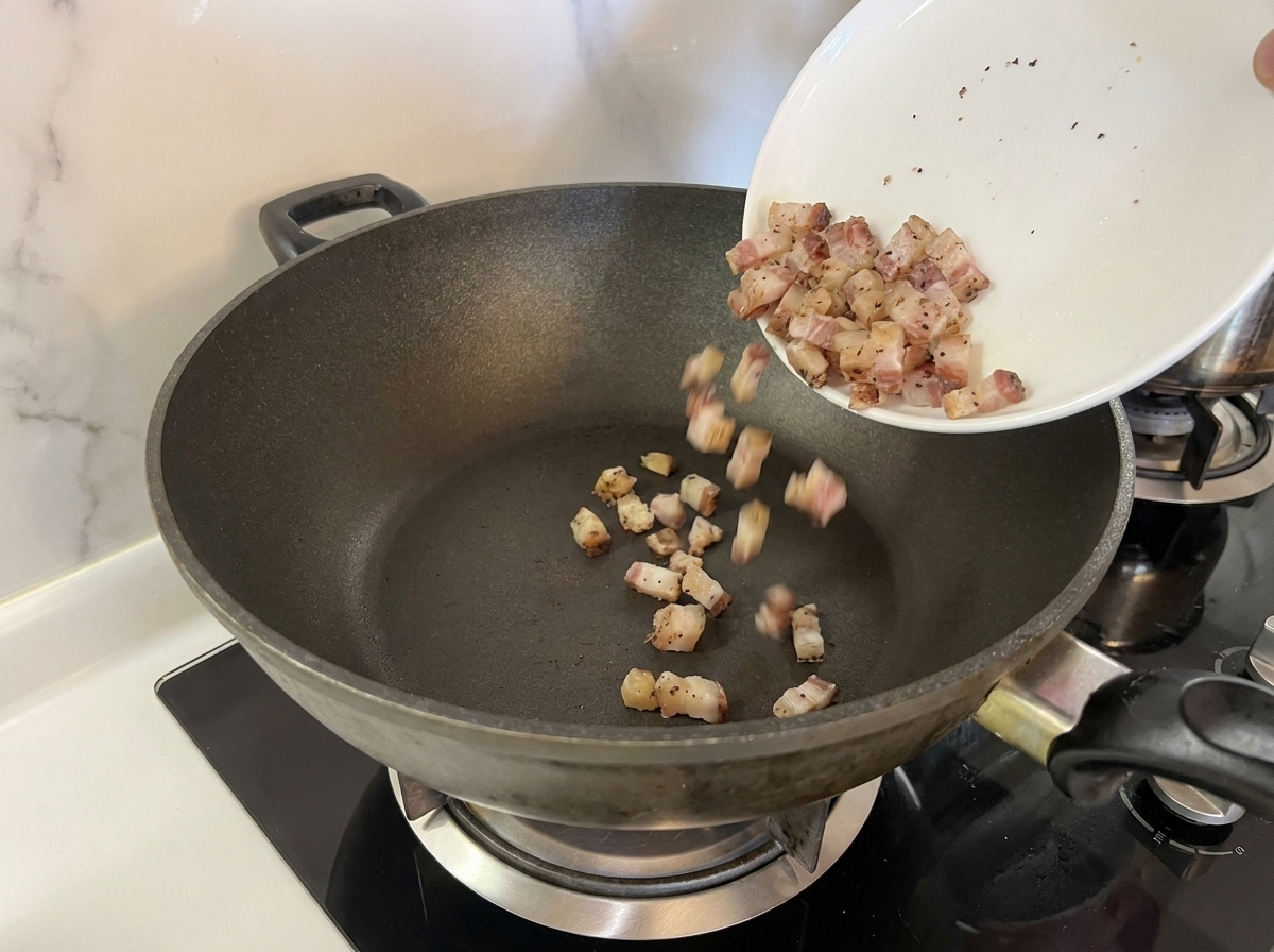 Cubes de guanciale versés dans une poêle sombre et sèche.