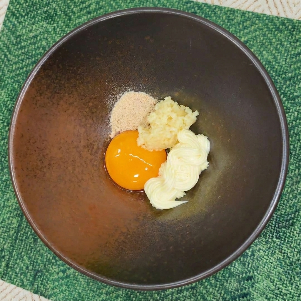 Poudre dassaisonnement pour ramen ajoutée dans un bol avec œuf, ail et mayonnaise.