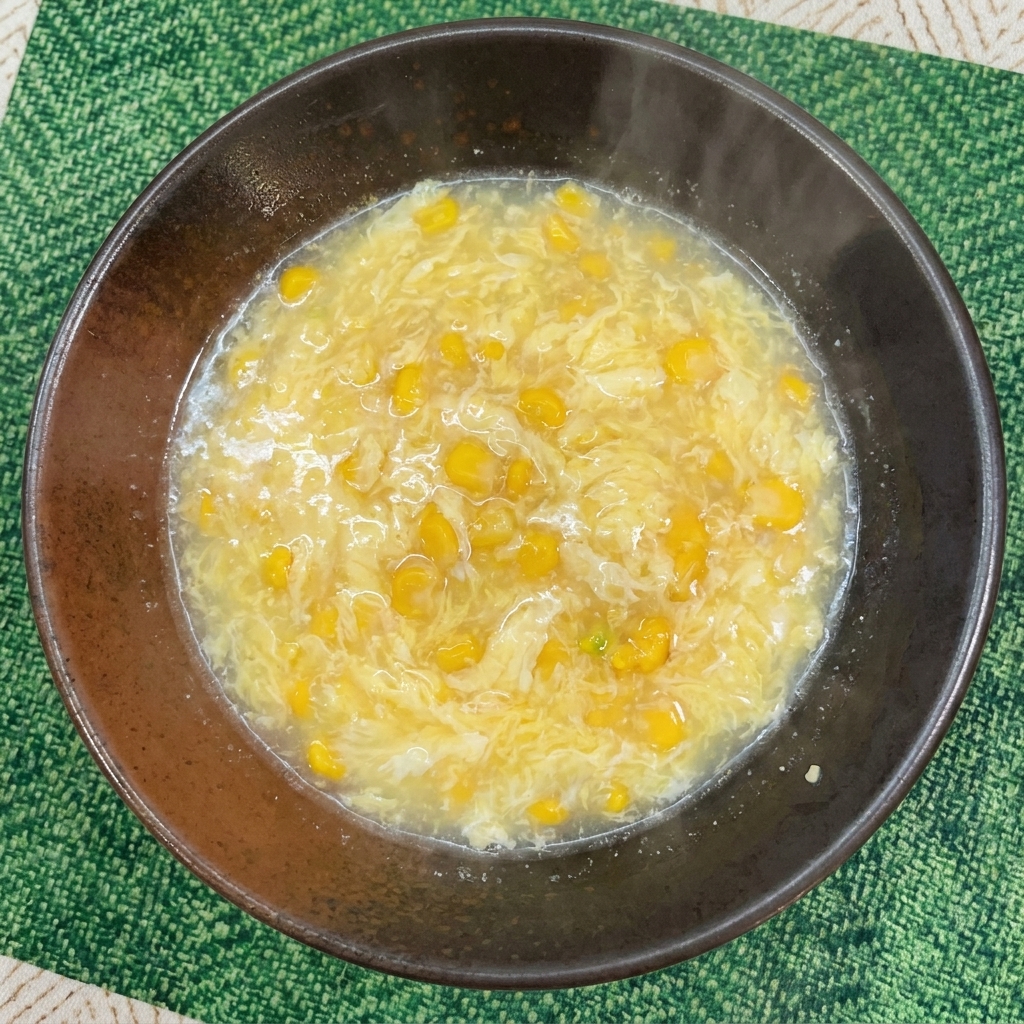 Un bouillon jaune clair mélangé avec des grains de maïs dans un bol de service sombre.