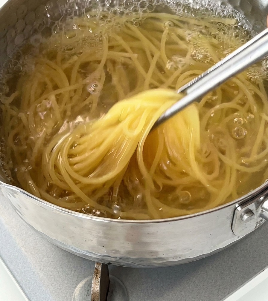 Gros plan de spaghettis soulevés dune casserole deau bouillante à laide dune pince métallique.