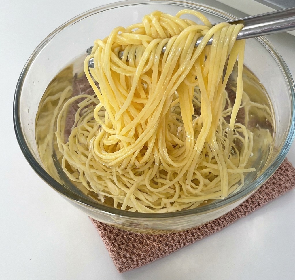 Une pince soulevant un nid de spaghettis cuits dun bol en verre rempli deau froide.