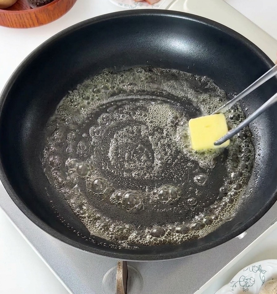 Une noisette de beurre jaune fondant et moussant dans une poêle antiadhésive noire.